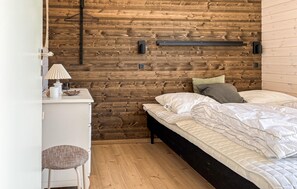 A bedroom with a wooden wall, a bed with white bedding, a bedside table with a lamp, and a hanging light fixture. - 3 bedroom beautiful home in Fjerritslev (Fjerritslev)