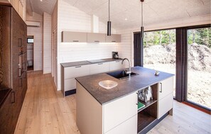 A modern kitchen with a central island, a built-in oven, and a large window offering a view of the outdoors.