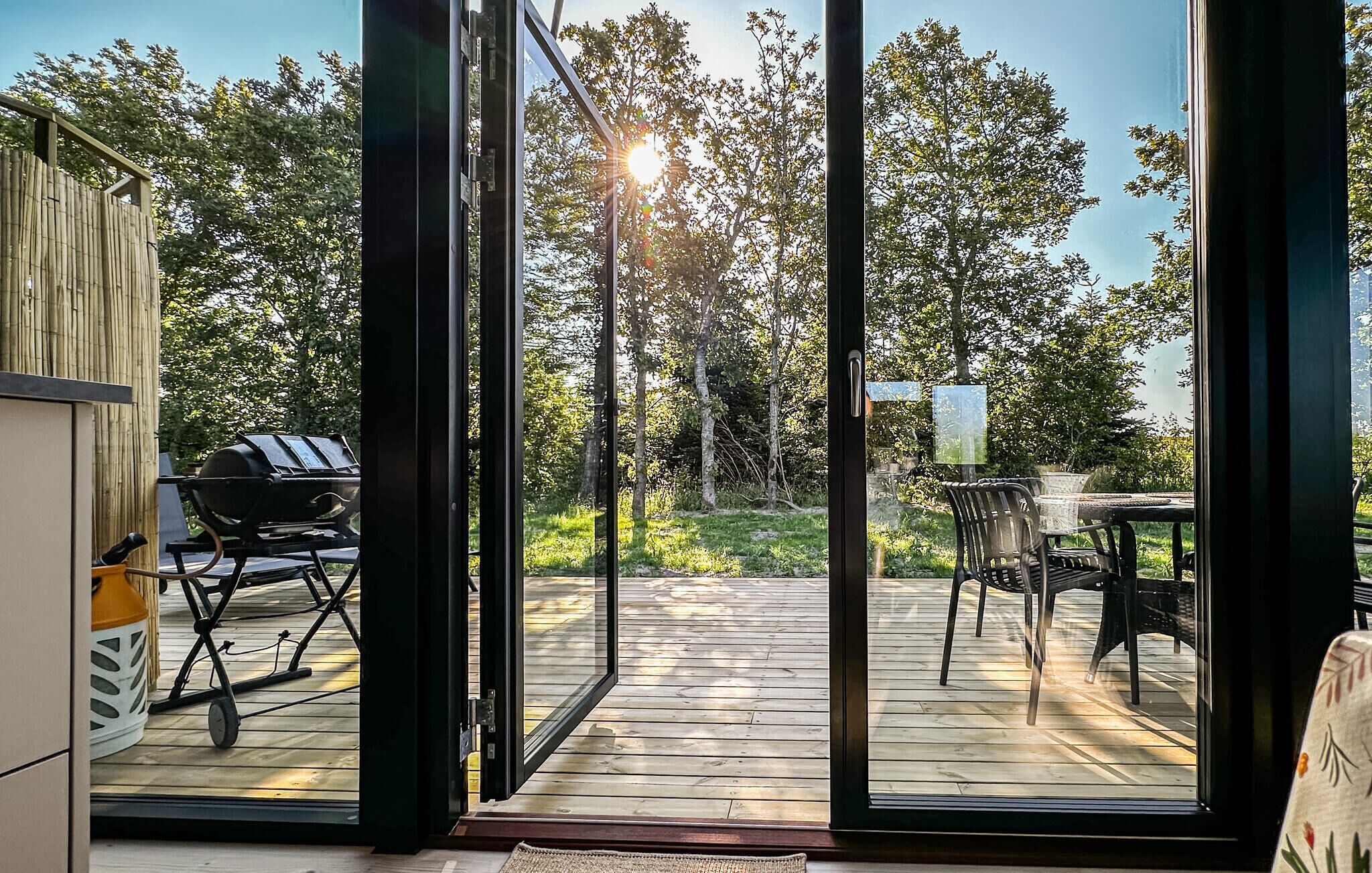 Une terrasse extérieure moderne, dotée d’un barbecue et d’un espace repas, le tout entouré d’arbres.