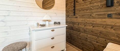 A room with a white dresser, a round mirror, a small stool, and a wooden wall.