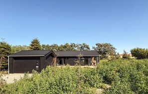 Zwei dunkle Holzhäuser mit blauem Himmel und Grün im Hintergrund.