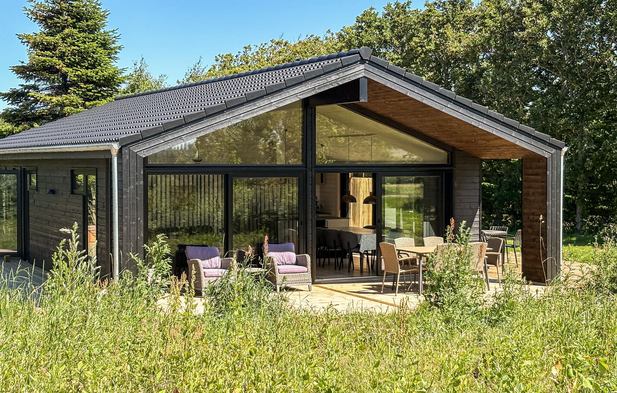 Una casa moderna con amplios ventanales, comedor con mobiliario exterior y un jardín.
