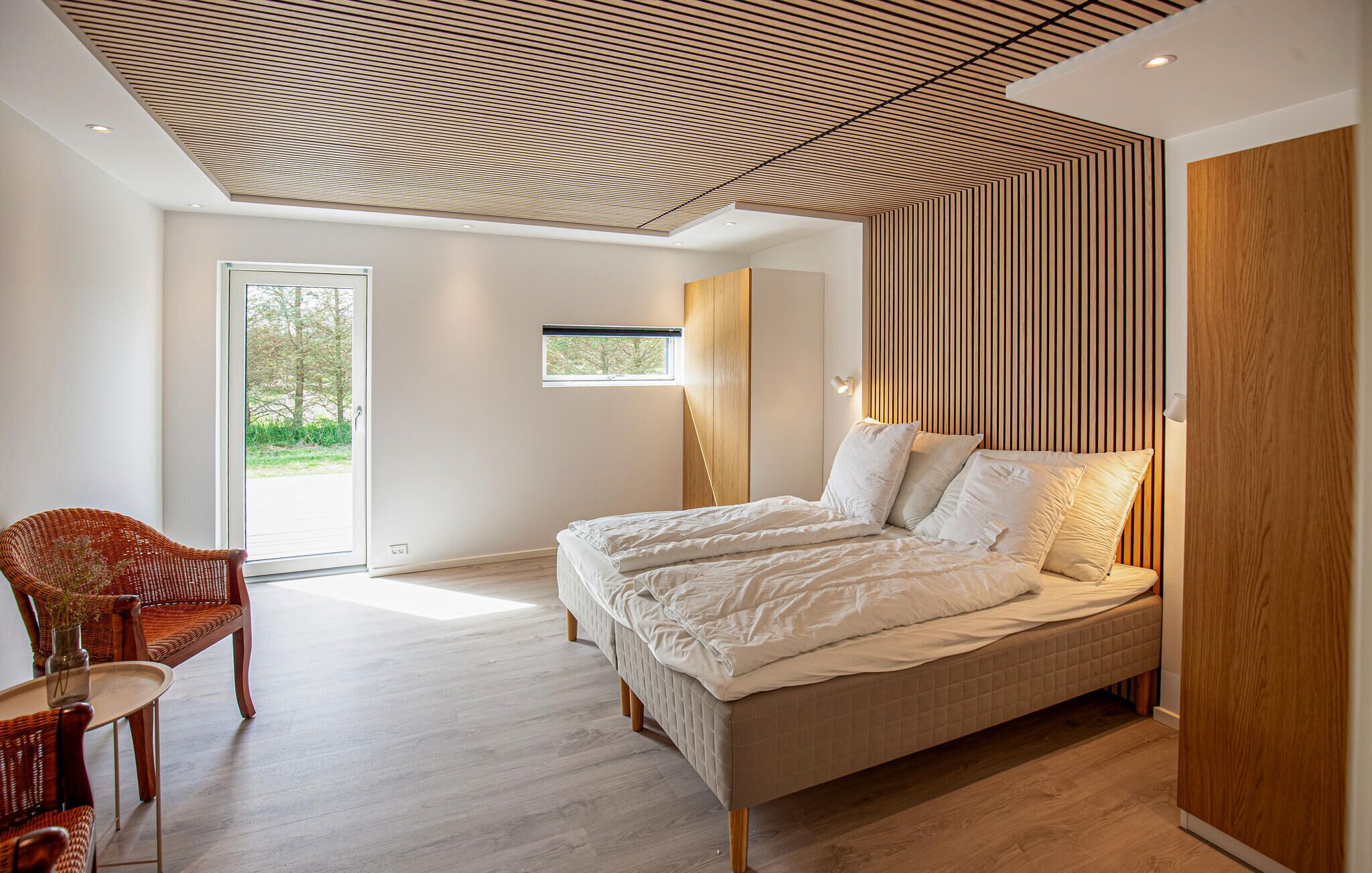 Une chambre avec un grand lit, une armoire en bois, une chaise en osier et une petite fenêtre.