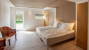 A bedroom with a large bed, a wooden wardrobe, a wicker chair, and a small window. - Gorgeous home in Sæby with sauna (Sæby)