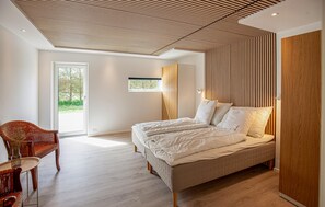 A bedroom with a large bed, a wooden wardrobe, a wicker chair, and a small window. - Gorgeous home in Sæby with sauna (Sæby)