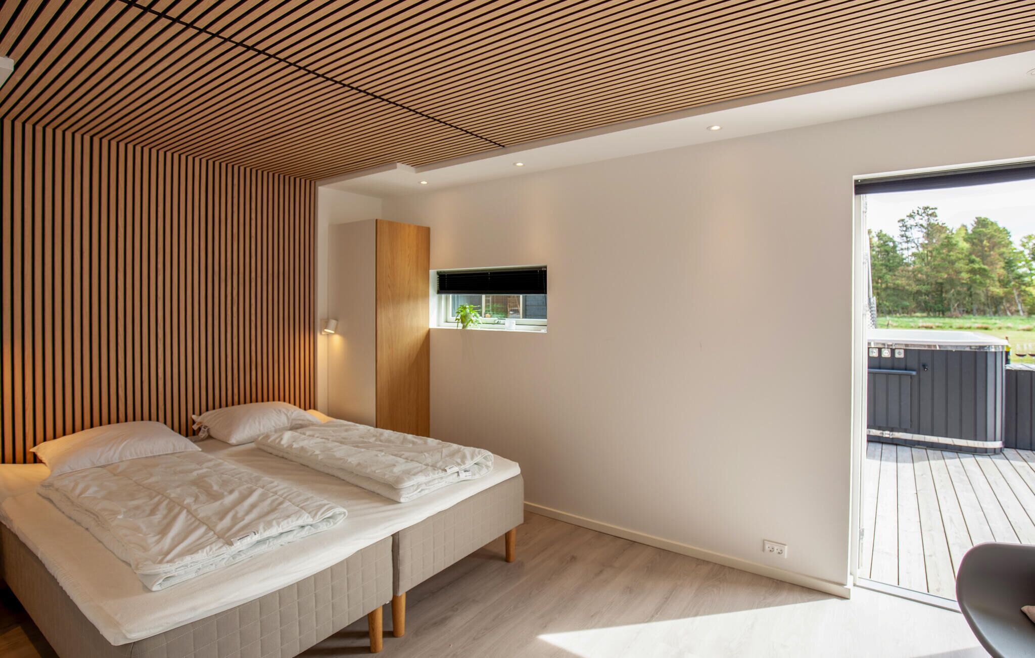Een moderne slaapkamer met een groot bed, een houten lattenplafond, een klein raam en uitzicht op de omgeving.