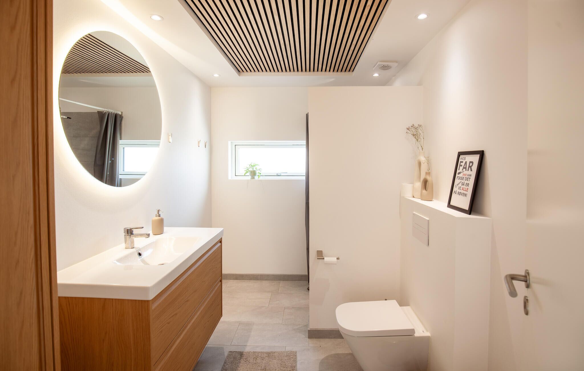 Un bagno moderno con uno specchio rotondo, un lavandino bianco, un water e uno spazio doccia.