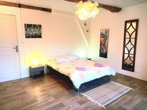 A bedroom with a bed, bedside lamps, a wooden floor, a door, and artwork on the walls.