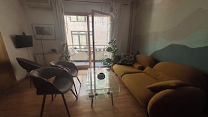 A living room with a sofa, chairs, a glass coffee table, a TV, and a view through a door. - Cozy apartment in a vibrant neighborhood  with fast internet (Skopje)