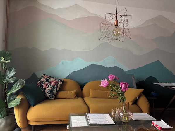 Una sala de estar moderna con un sofá, una mesa de centro con papeles, un jarrón con flores y un mural en la pared.