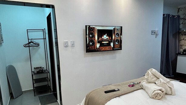 Ein modernes Schlafzimmer mit einem Bett, einem an der Wand montierten Fernseher, einem Deckenventilator und einer Tür zu einem anderen Raum.