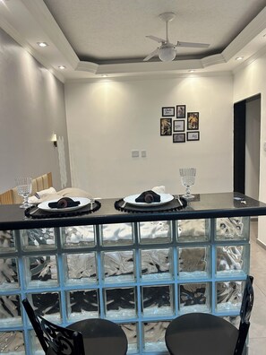 Un espace repas moderne avec une table à plateau en verre, des chaises noires et un ventilateur de plafond.