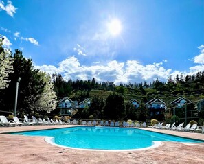 Una piscina con sillones de descanso, rodeada de casas y árboles bajo un cielo despejado.