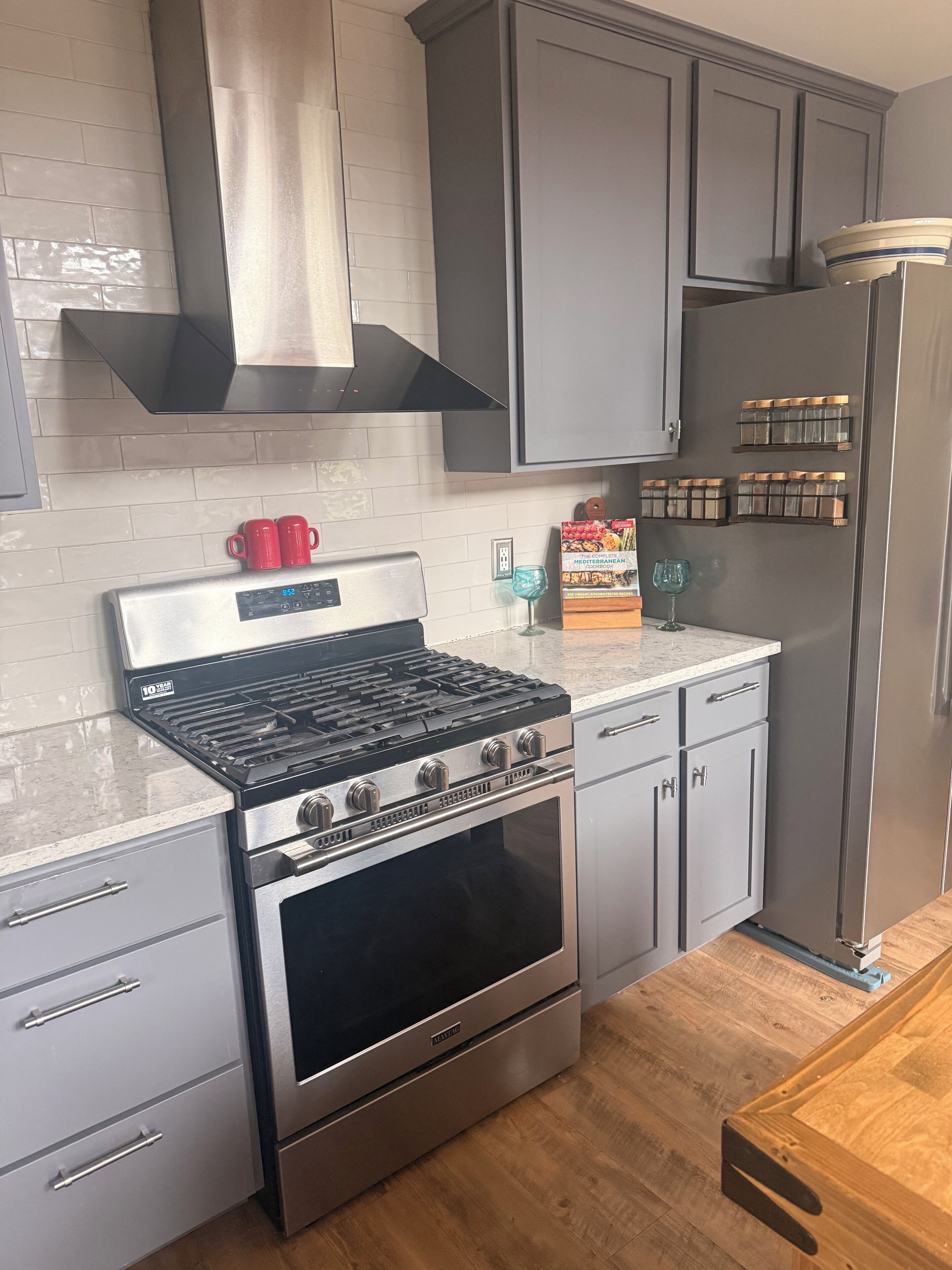 A kitchen with a gas stove, oven, grey cabinets, and a refrigerator.