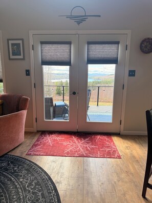 Ein Zimmer mit einer Schiebetür und Zugang zu einer Terrasse, einem roten Teppich, einem gemusterten Teppich und einem Sessel.