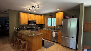A kitchen with wooden cabinets, a stainless steel refrigerator, a microwave, and a granite countertop. - Charming 3-bedroom cabin in Woodruff perfect for relaxing getaways (Woodruff)