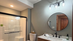 A modern bathroom with a glass-enclosed shower, a toilet, a sink with a marble countertop, and wooden cabinets. - Charming 3-bedroom cabin in Woodruff perfect for relaxing getaways (Woodruff)