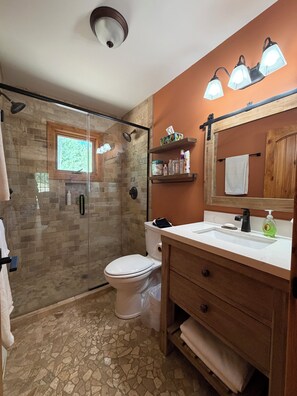 A bathroom with a glass shower enclosure, a white toilet, a vanity with a mirror, and a sink.