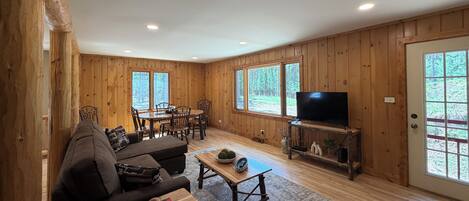 A wooden-paneled room with a dining area, a sofa, a coffee table, and a television.