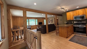 A spacious kitchen with wooden cabinets, a large island, and a dining area with a wooden railing. - Charming 3-bedroom cabin in Woodruff perfect for relaxing getaways (Woodruff)