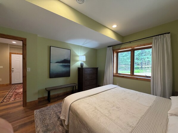 A bedroom with a bed, a dresser, a bench, a painting, and a window with curtains. - Charming 3-bedroom cabin in Woodruff perfect for relaxing getaways (Woodruff)
