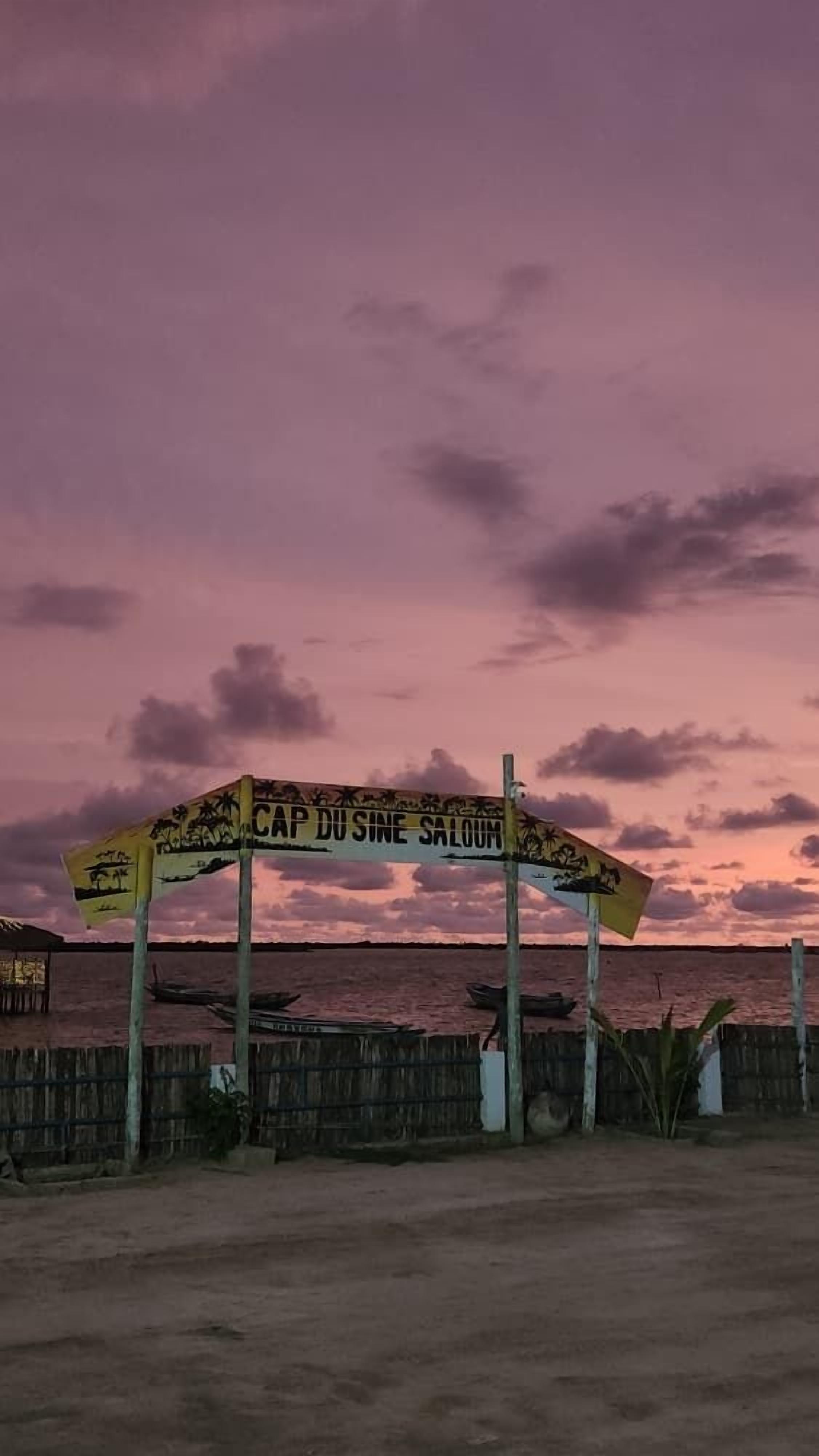 A sign with 'CAP DUSINE SALOM' written on it, set against a sunset sky.