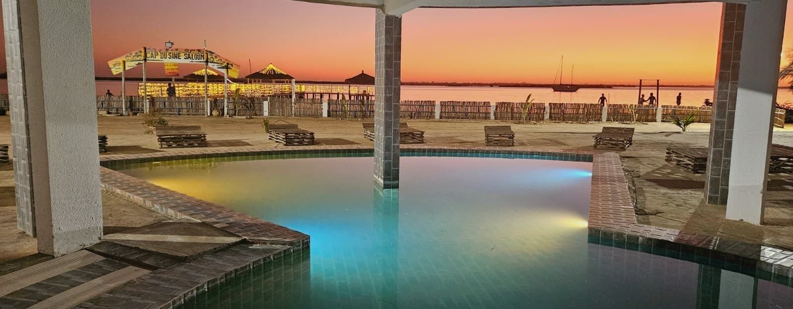 A pool area with a view of a pier and sunset.