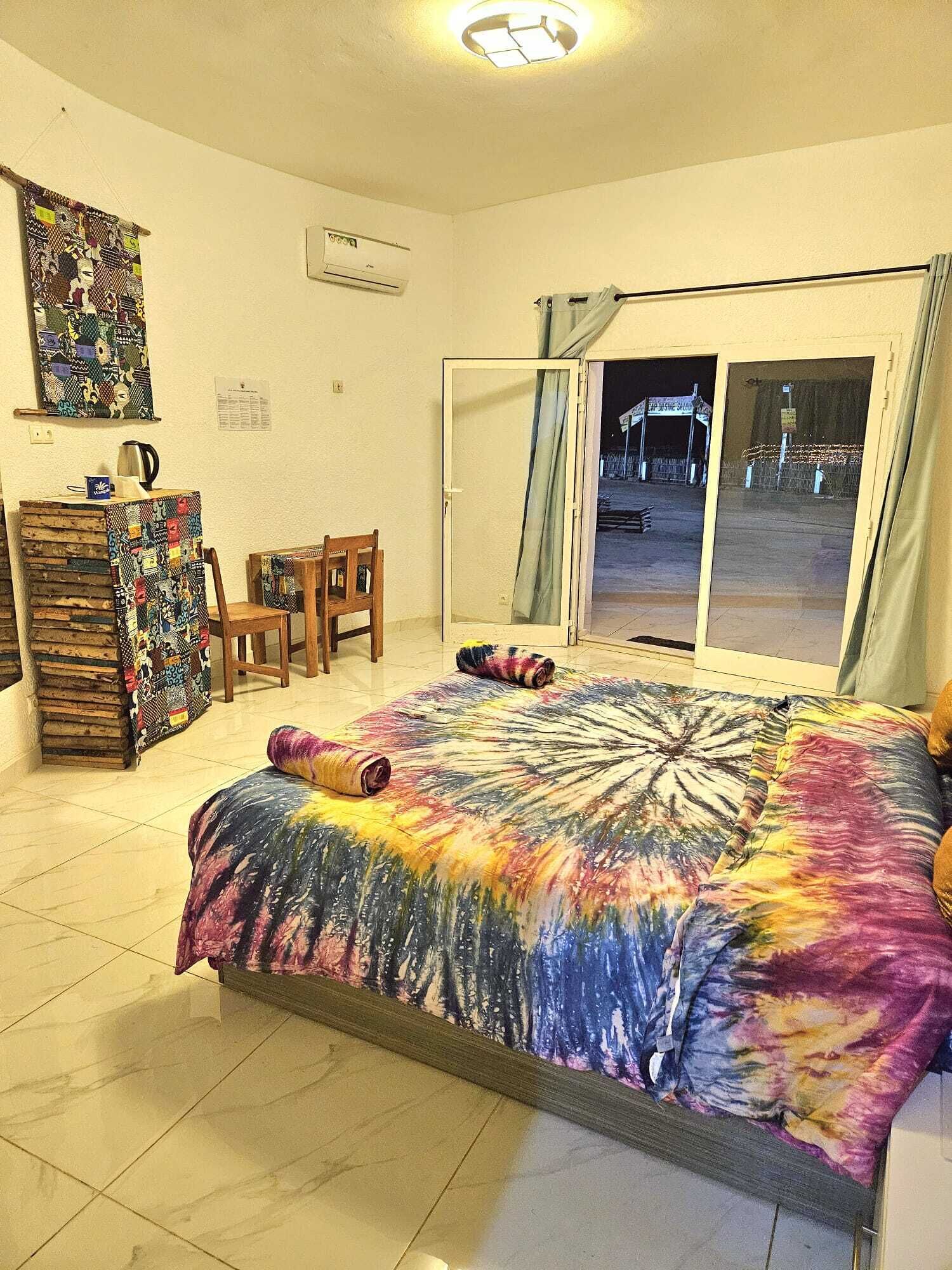 A room with a bed, a desk, a chair, a window with curtains, and a wall-mounted air conditioner.