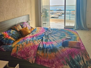 A bed with colorful bedding and a view of a marina through a glass door. - Hotel Cap du Sine Saloum (Fatick)