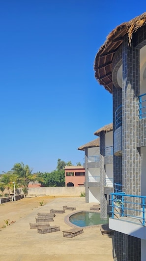 A hotel with a swimming pool, outdoor seating, and a clear blue sky.