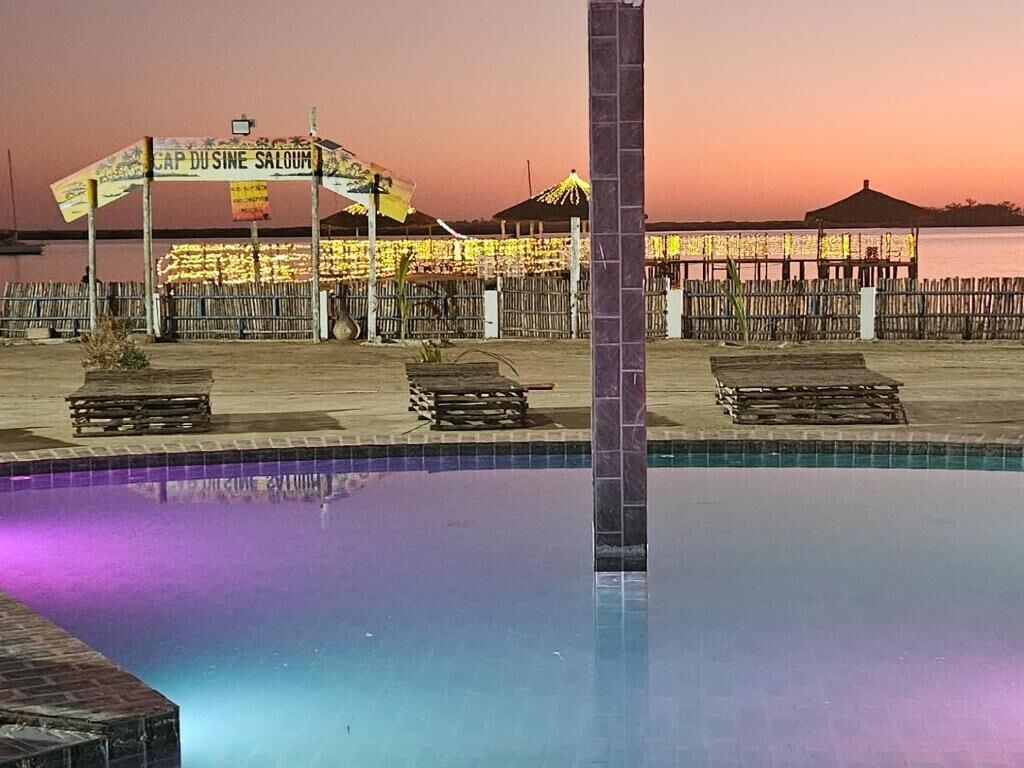 A swimming pool with a tiled edge, a wooden deck area, and a sign that reads 'CAP DUSINE SALOUM.'