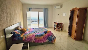 A bedroom with a bed, a chair, a wardrobe, and a view of the sea.