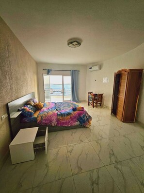 A bedroom with a bed, a chair, a wardrobe, and a view of the sea. - Hotel Cap du Sine Saloum (Fatick)