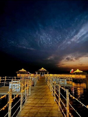 A wooden pier extending into a body of water, with railings and lights along the sides.