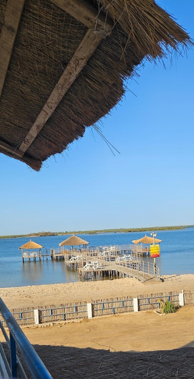 Une jetée dotée de structures à toits de chaume et d’une zone de plage sablonneuse.