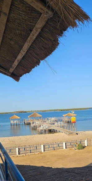 A pier with thatched-roof structures and a sandy beach area. - Hotel Cap du Sine Saloum (Fatick)