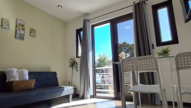 Een moderne woonkamer met een bank, een eettafel met stoelen, een groot raam met gordijnen en een potplant.