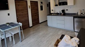 Een moderne keuken met witte kasten, een eethoek met tafel en stoelen, en een gezellige zithoek met een mand handdoeken.