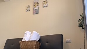 Een donkere bank met een gevlochten mand met daarin opgevouwen witte handdoeken, een potplant en een wandcontactdoos.