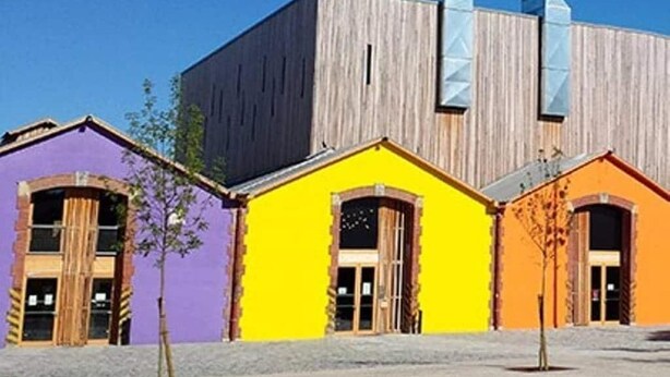 A building with a large wooden structure and three colorful houses in purple, yellow, and orange. - Roquepoix - A green stopover in the Gers (Mirepoix)