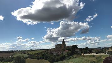 Un edificio storico con una torre, circondato da vegetazione e campi, sotto un cielo parzialmente nuvoloso.