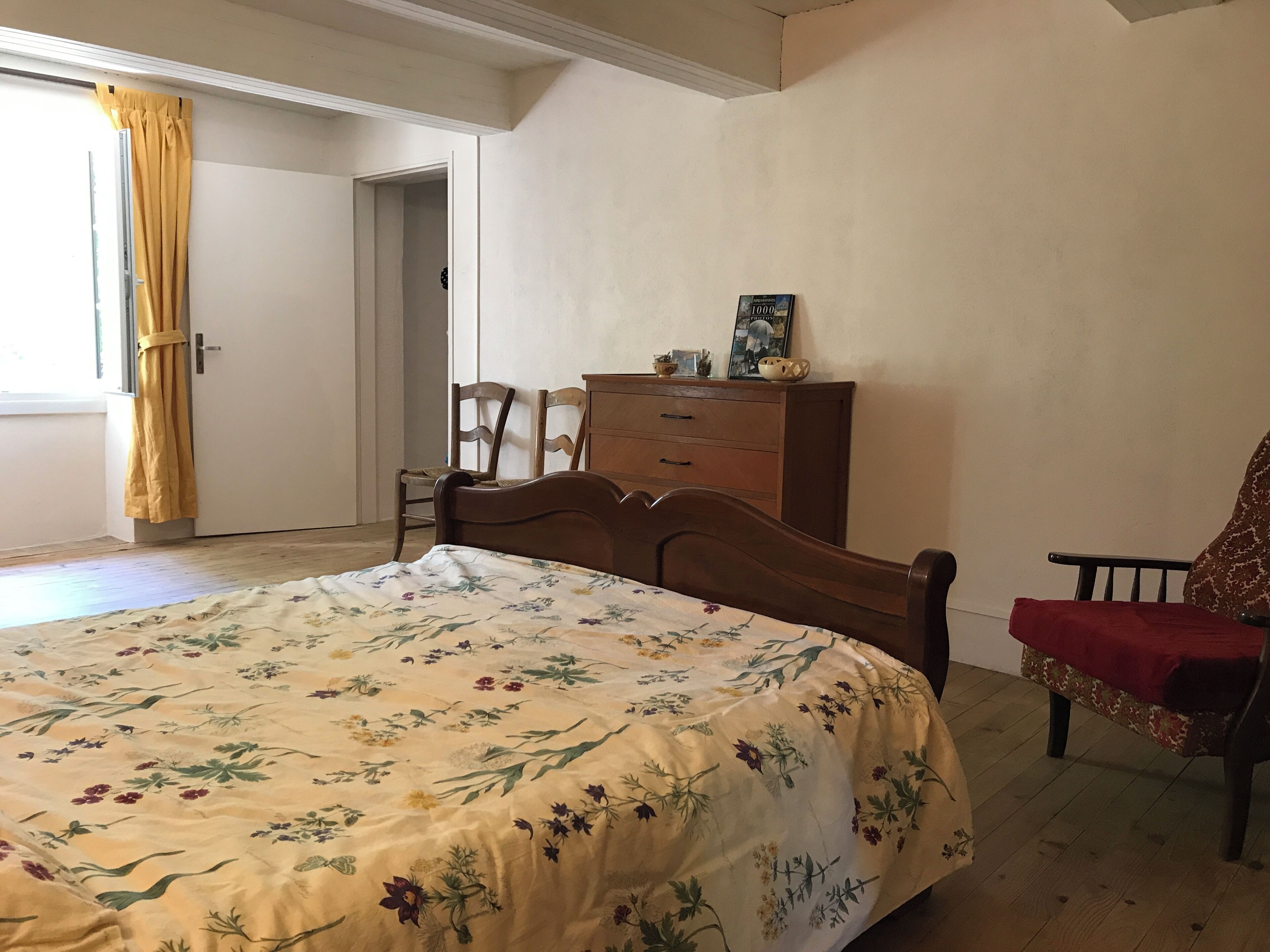 A bedroom with a bed, a wooden dresser, a chair, and a window with curtains.