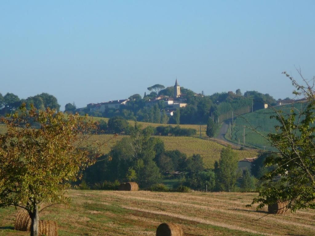 A rural landscape with rolling hills, hay bales, and a church on a hill.