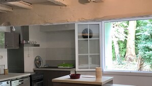 A kitchen with a washing machine, oven, and a window with a view of greenery. - Roquepoix - A green stopover in the Gers (Mirepoix)
