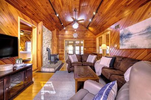 Interior de una cabaña de troncos con techo de madera, chimenea, sofá y televisor.