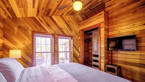 Ein Schlafzimmer einer Holzhütte mit einem Bett, einem Deckenventilator, einem Fernseher und einem Fenster.