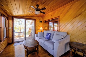 A wooden interior with a sofa, two tables, a ceiling fan, and a view through a glass door.