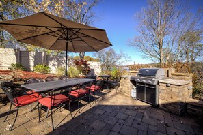 Une terrasse extérieure avec une table et des chaises, un barbecue et un parasol.