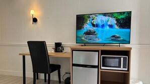 A modern room with a wooden desk, a black chair, a television displaying a waterfall scene, a coffee maker, a mini-fridge, and a microwave. - Tumbleweed Motel  (Cache Creek)