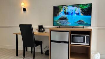 A modern room with a wooden desk, a black chair, a television displaying a waterfall scene, a coffee maker, a mini-fridge, and a microwave.